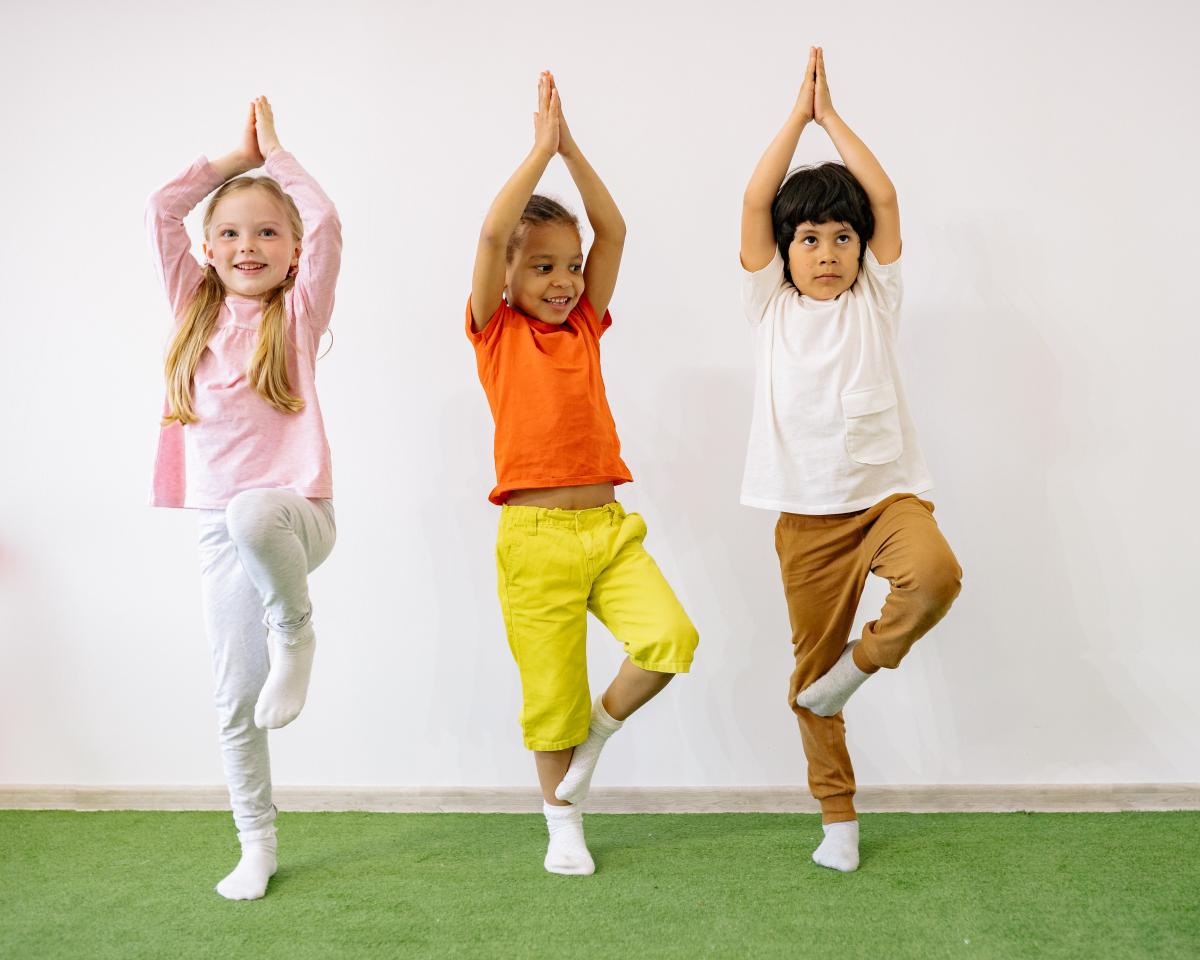 Drie kinderen staan op een rij en doen een yoga positie.