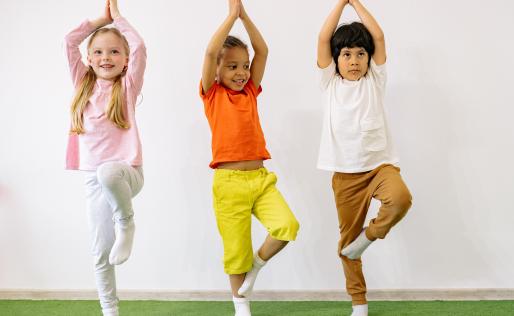 Drie kinderen staan op een rij en doen een yoga positie.