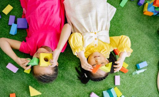 Twee kinderen liggen op de grond en spelen met blokken voor hun ogen.