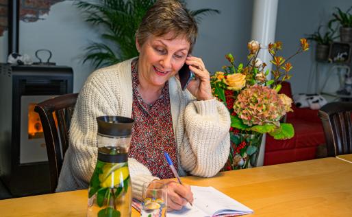 Mevrouw zit aan de keukentafel en belt