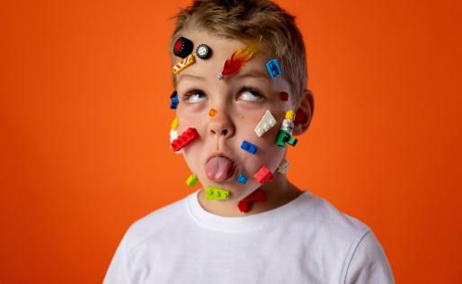 Een jongetje met lego op zijn gezicht geplakt steekt zijn tong uit.